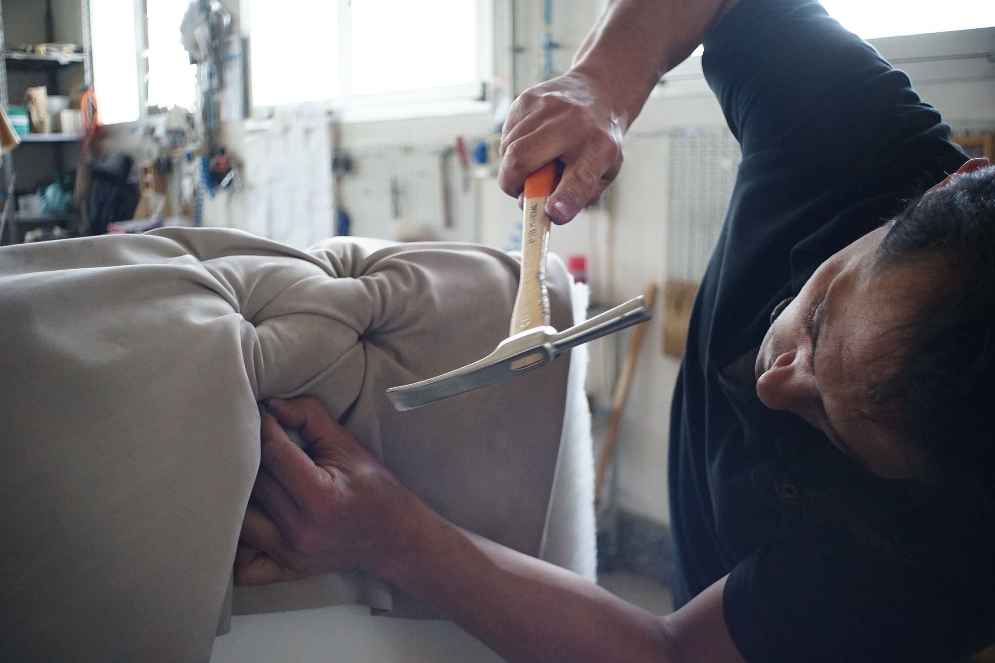 Polsterer bei der handwerklichen Arbeit mit Polsterhammer an einem gepolsterten Möbelstück